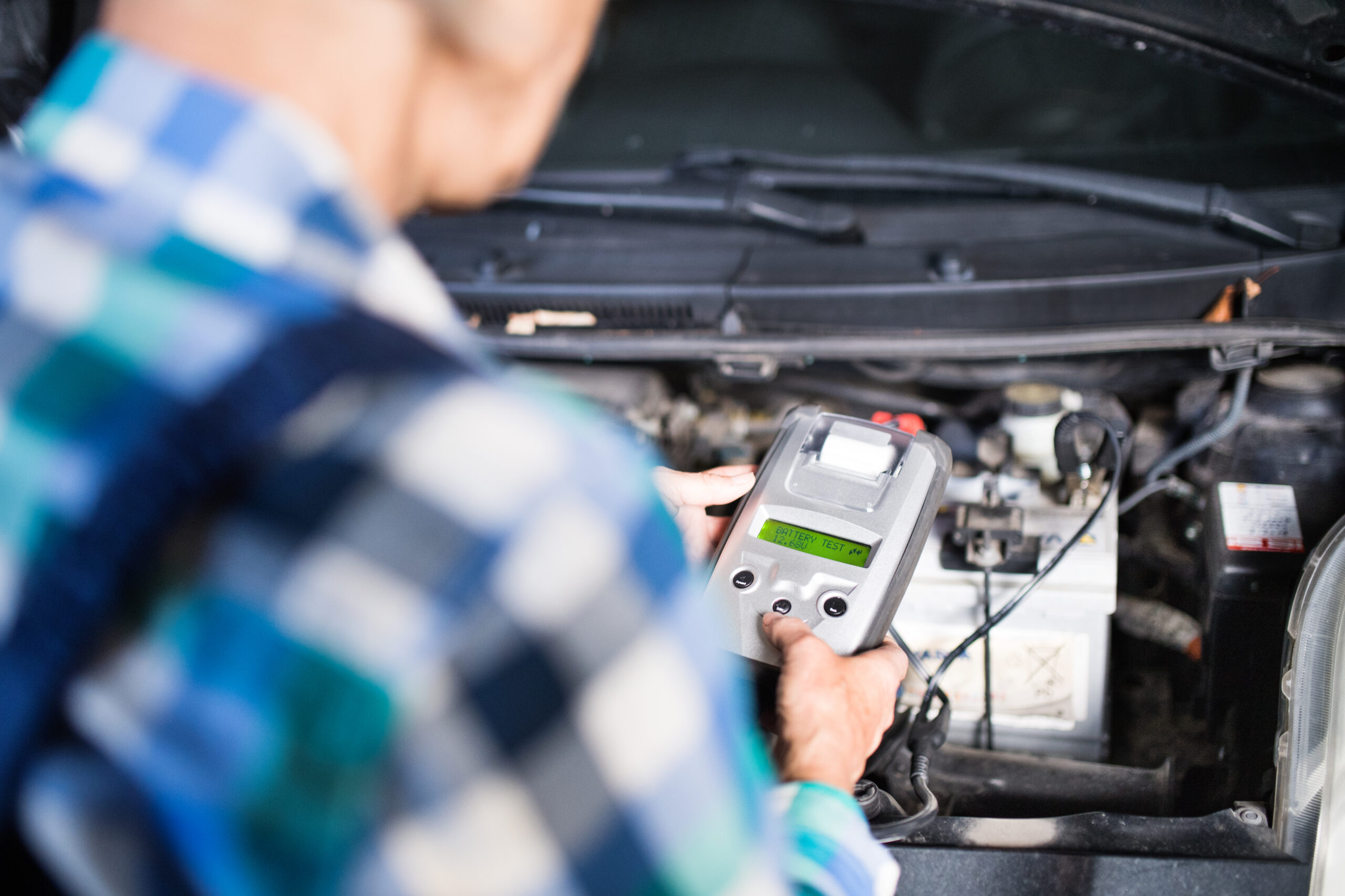 Mechanic testing car battery voltage with tester tool